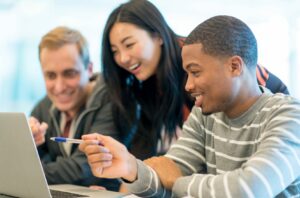 Three students smiling and pointing at laptop screen.