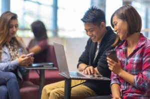 Two students smiling and looking at laptop screen in a student lounge.